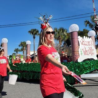 A woman in a red shirt and reindeer antlers is walking in a parade.