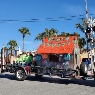 A group of people are riding on the back of a trailer with a small house on it.