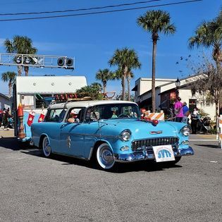 A blue car is driving down a street with palm trees in the background.
