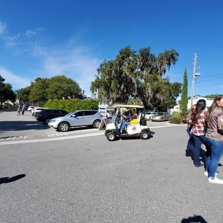 A group of people are walking down a street next to a golf cart.