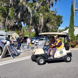 Two lions club members are riding a golf cart down a street.