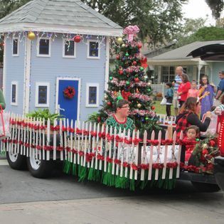 A christmas parade with a float that looks like a house with a christmas tree on it.