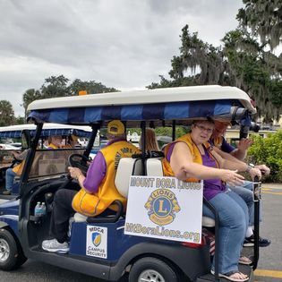 A group of people are riding in a golf cart with a lion 's club sign on the back.