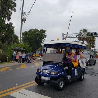 A golf cart is driving down a street in the rain.