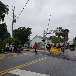 A group of people are walking down a street in front of a railroad crossing.