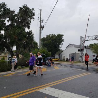 A group of people are crossing a street near a train crossing.