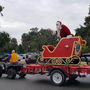 A man is riding an atv pulling a sleigh with santa claus in it.