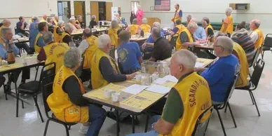 A group of people wearing yellow vests are sitting at tables.