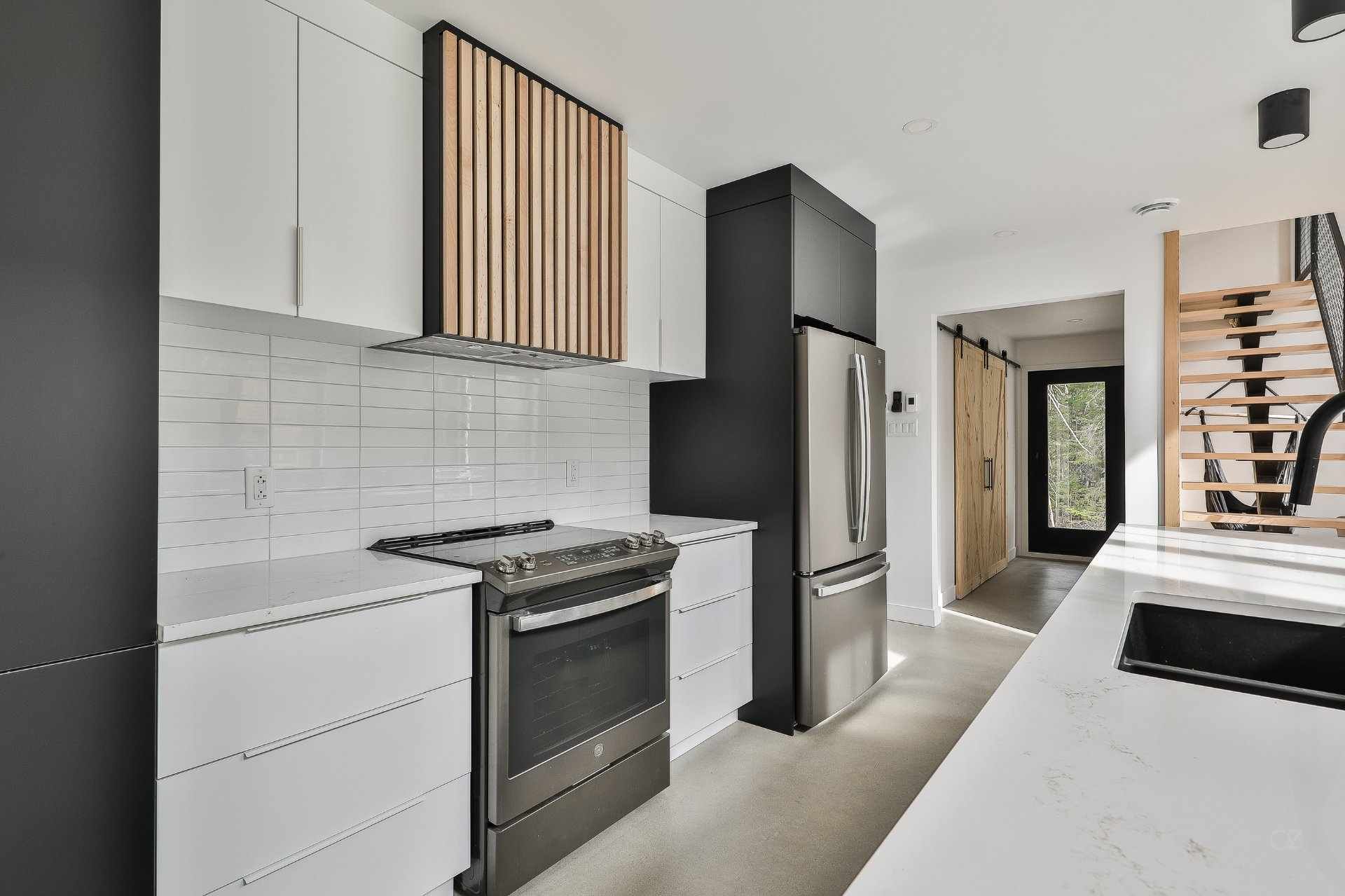 Une cuisine avec des armoires blanches, des appareils électroménagers noirs, un réfrigérateur et un évier.