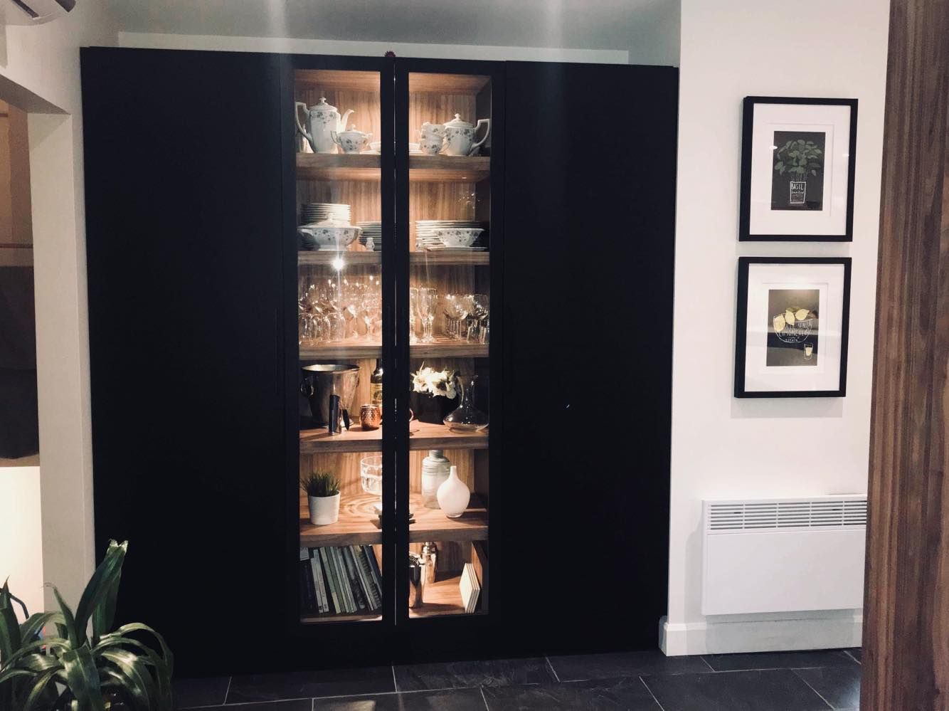 Une armoire noire avec des portes vitrées est remplie d'assiettes et de verres.