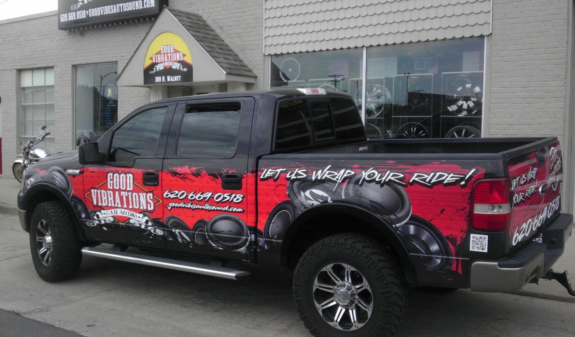 A truck with a wrap on it is parked on the side of a road.