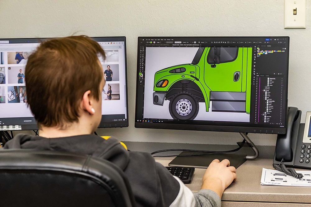 A man is sitting at a desk looking at a green truck on a computer screen.