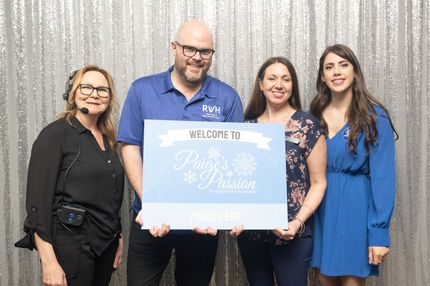 Four people pose in front of a silver backdrop, holding a blue sign that says 