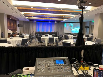 Conference room setup with soundboard, tables, screen, and stage lighting.