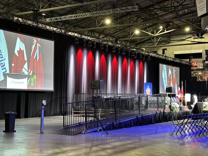 Stage setup with black backdrop, red and white lights, podium, and ramp.