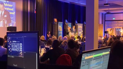 People at a business awards event, with speakers on stage and screens in the foreground.