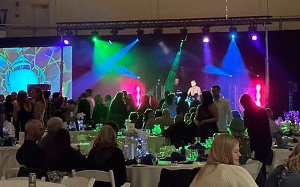 Band performing on stage with colorful lights, audience at tables in a large hall.