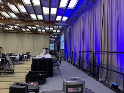Conference room set up with tables, stage, blue lighting, and gray curtains.