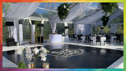 Clear tent wedding reception with black dance floor, white draping, and tables set for guests.