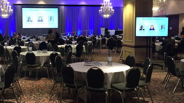 Conference room with round tables, chairs, screens, and blue lighting.