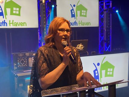 Woman speaking into a microphone at a podium, South Haven logo in background.