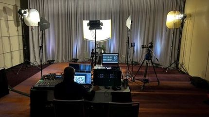Filming studio setup: Technician at workstation, cameras, lights, backdrop.