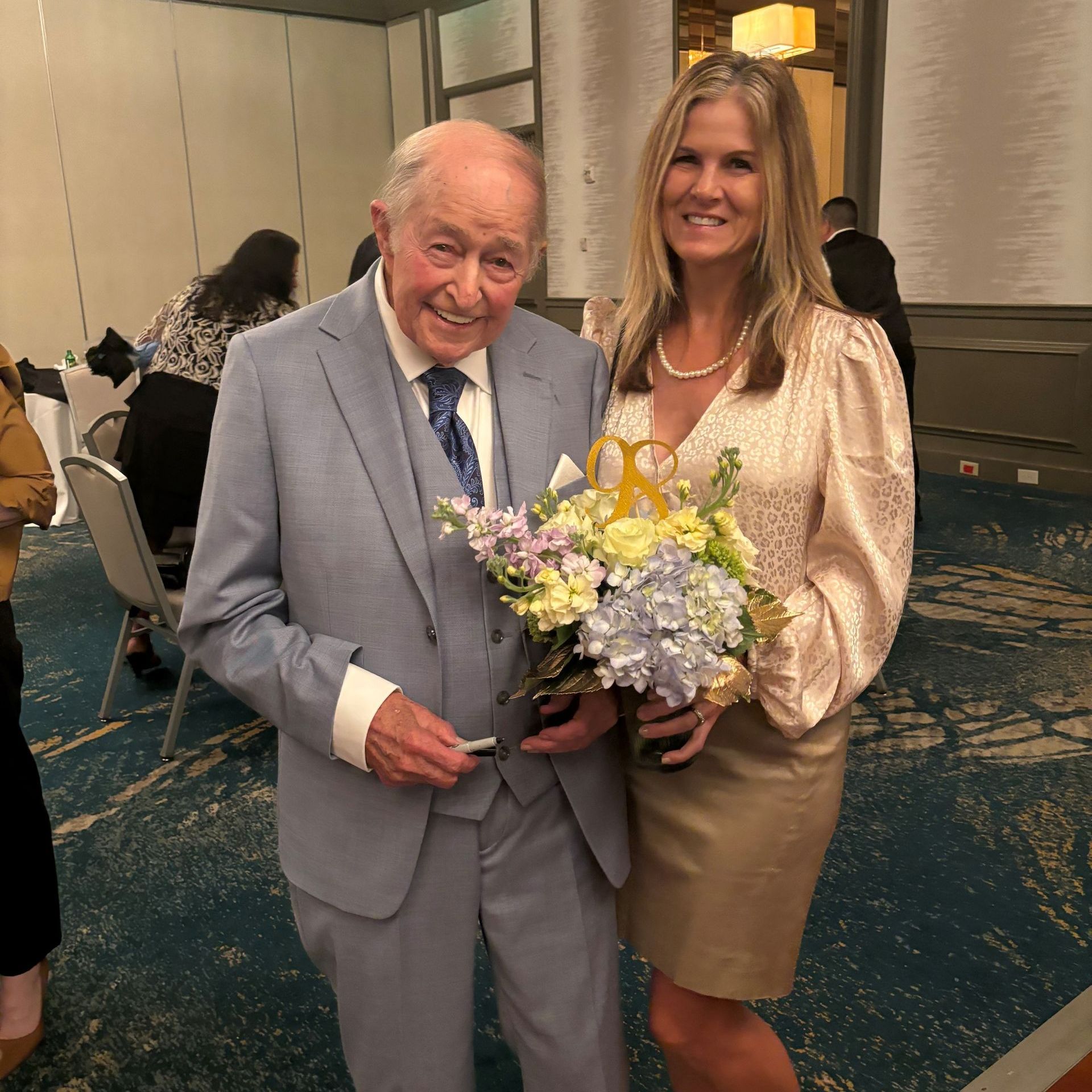 A man in a suit and tie is standing next to a woman holding flowers.