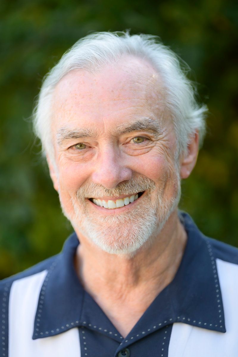 Man in glasses and suit smiles, tie with colorful abstract design.