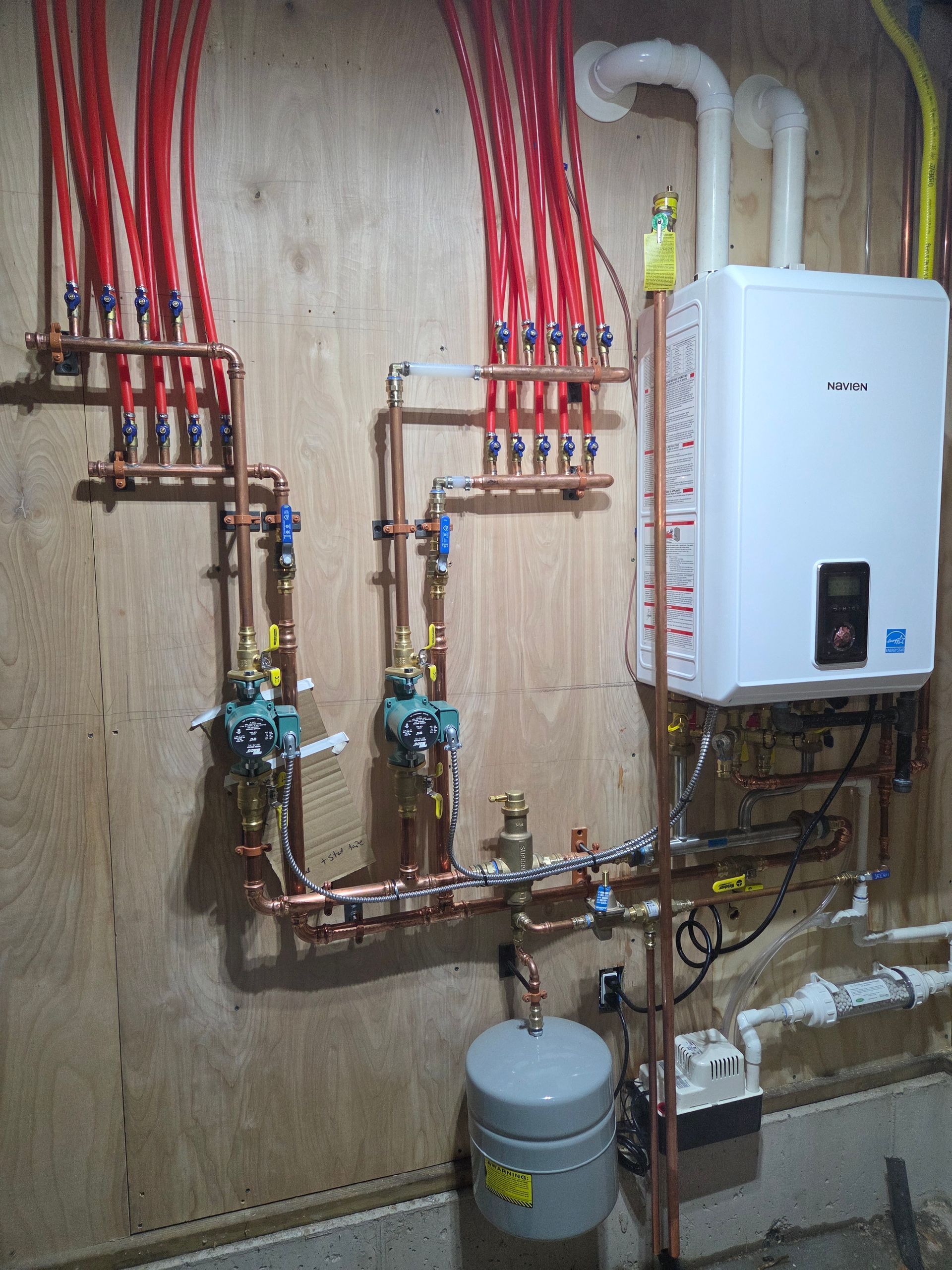 Copper pipes and a white water heater mounted on a wooden wall; radiant heat system.