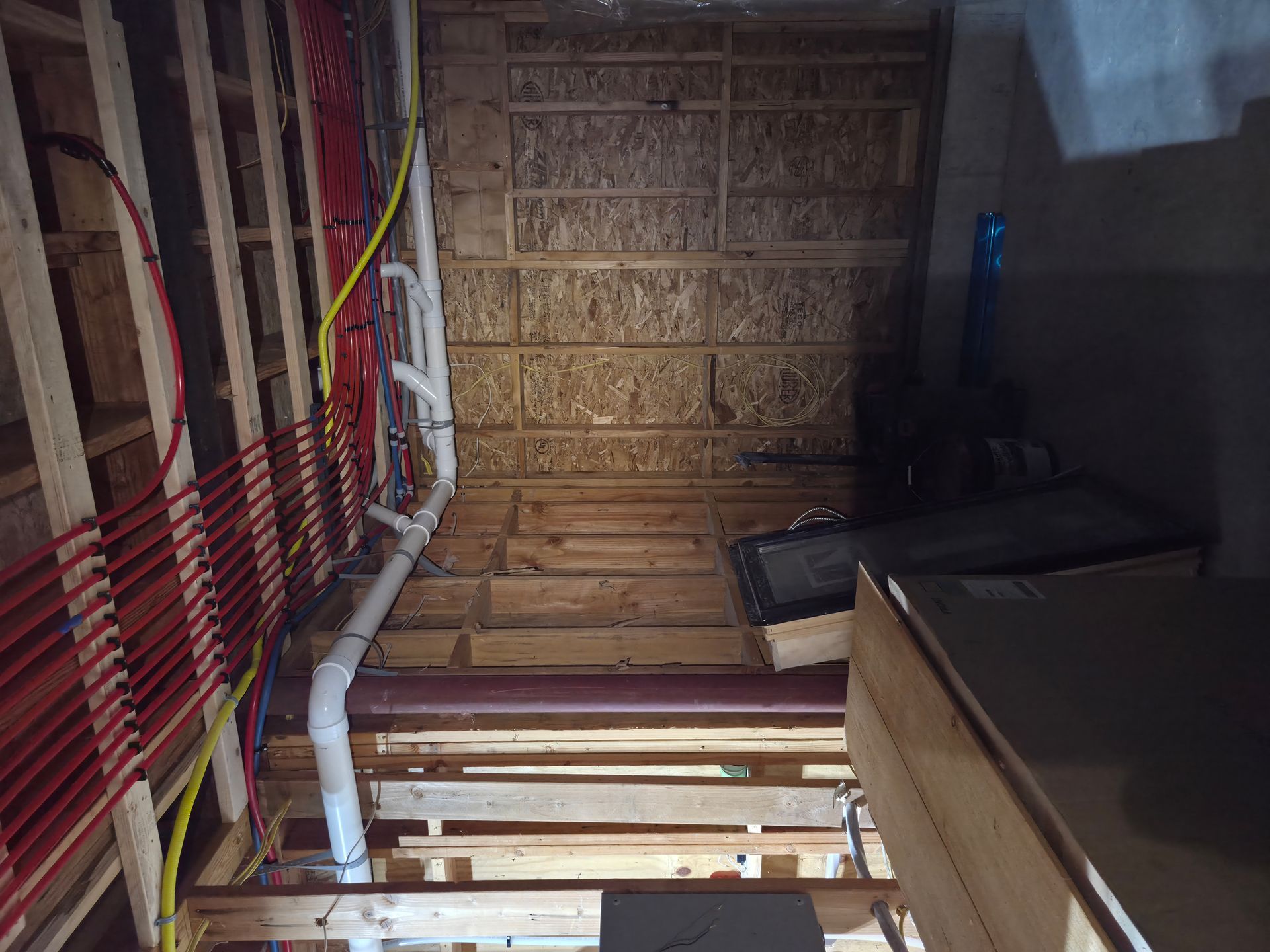 Interior view of a partially constructed space with exposed studs, pipes, and wiring.