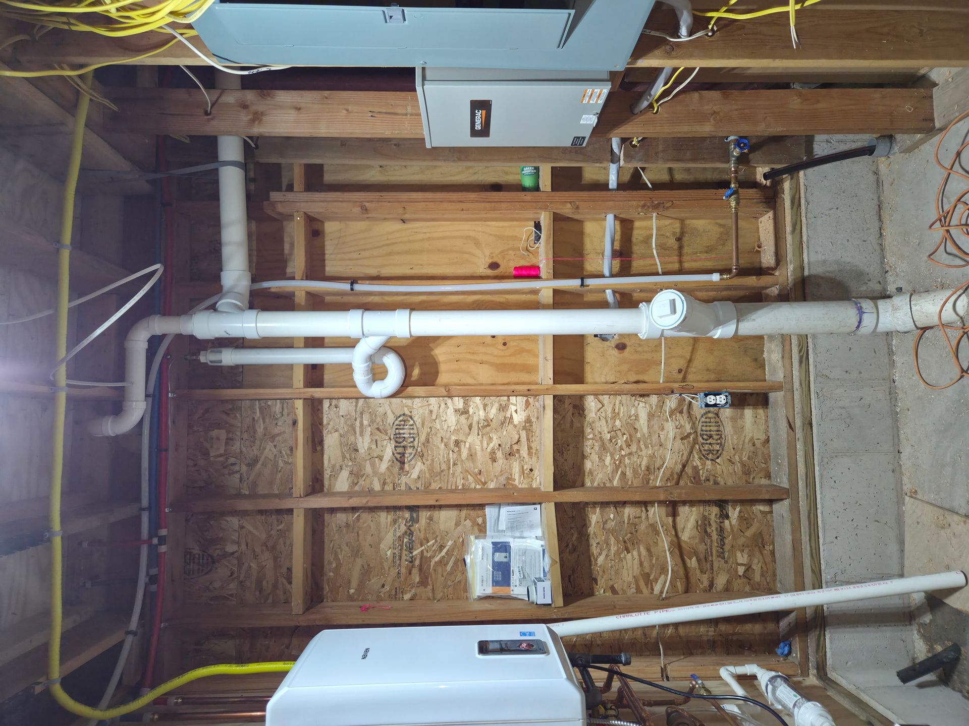 Plumbing and electrical work in a basement. White pipes run horizontally and vertically against wood studs and concrete.