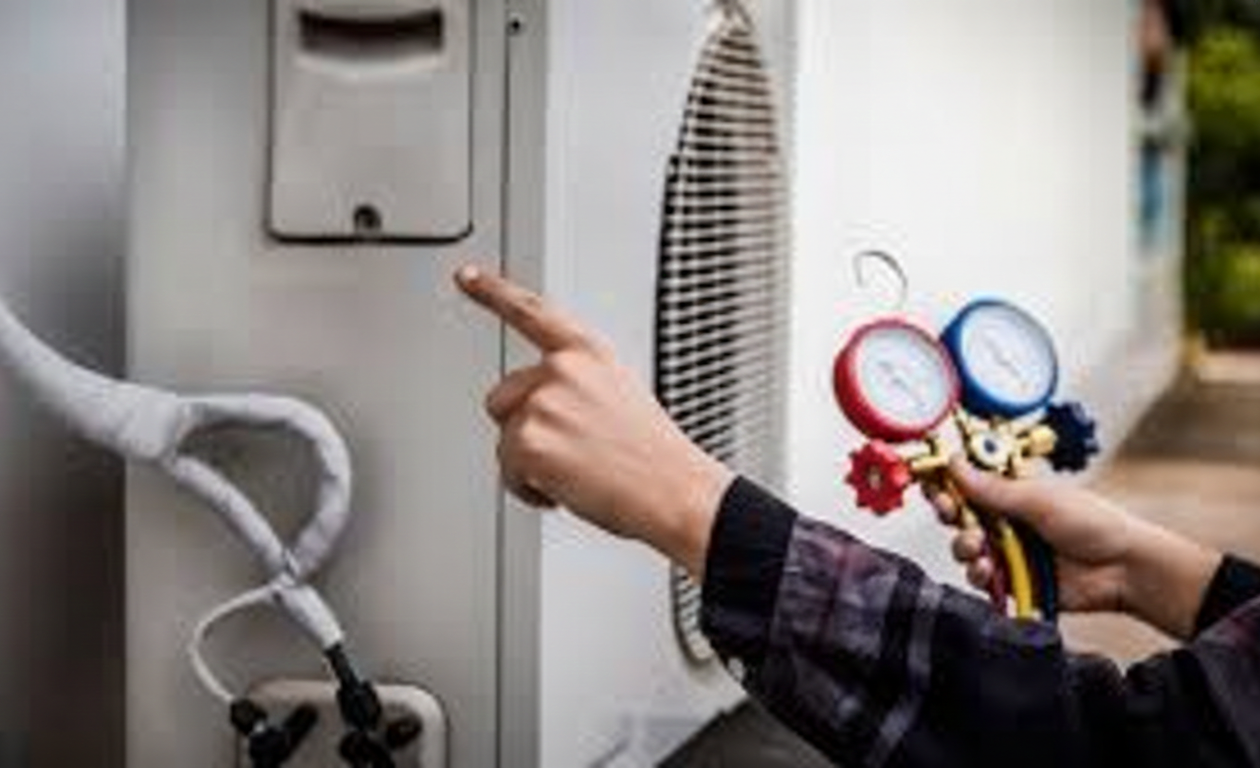 Person points to an air conditioner unit while holding gauges.