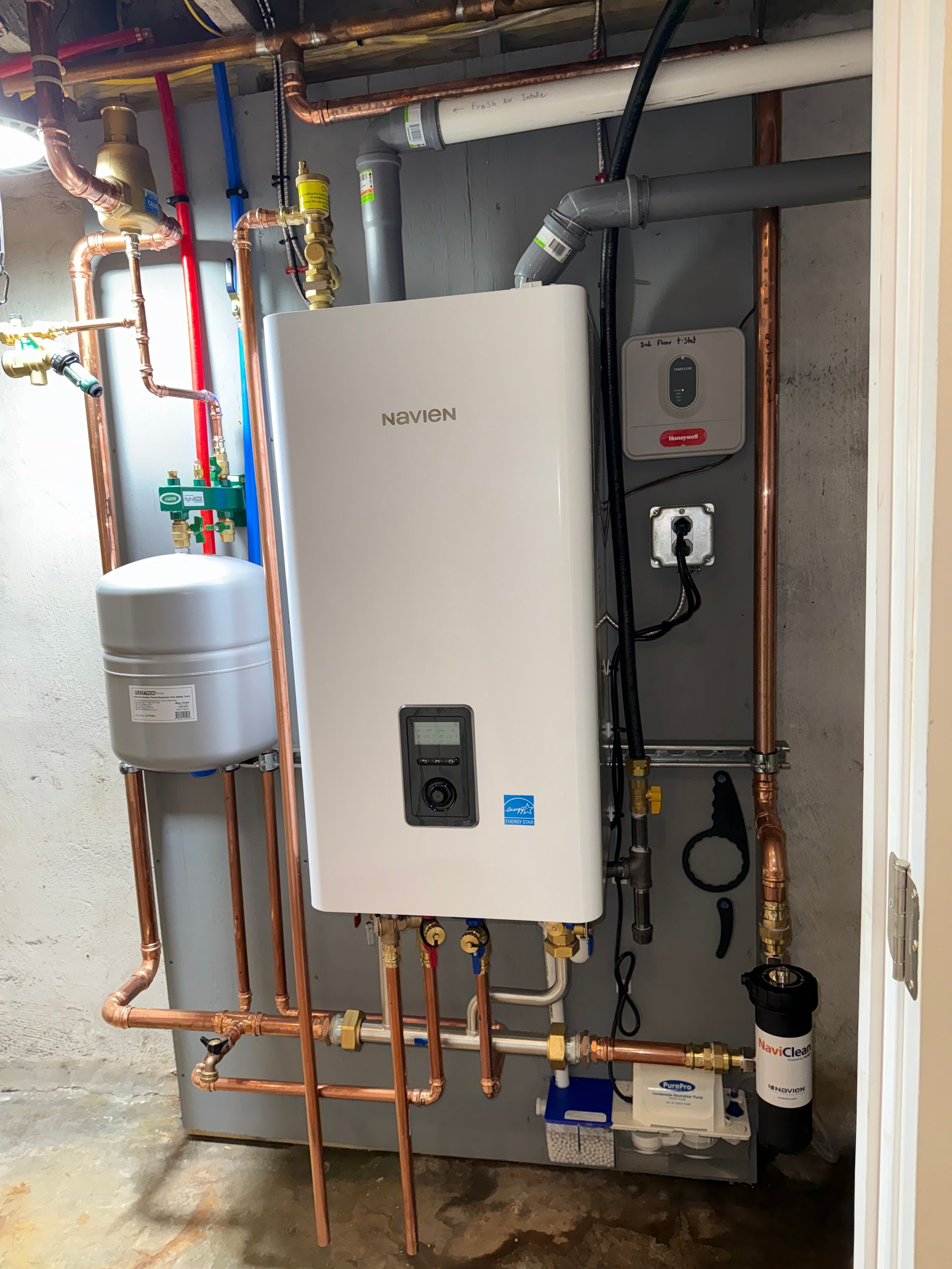 White tankless water heater with copper pipes in a utility room.