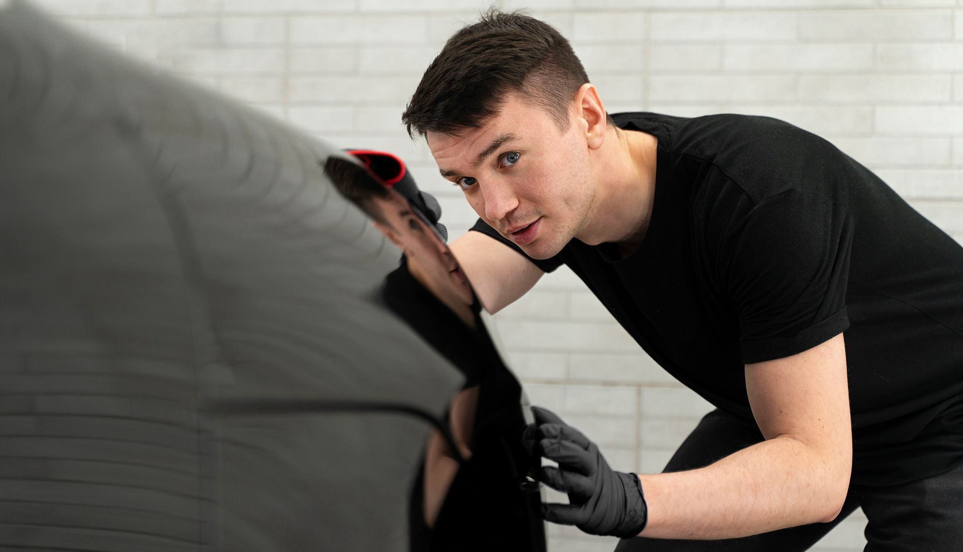A man is cleaning a black car with a cloth.