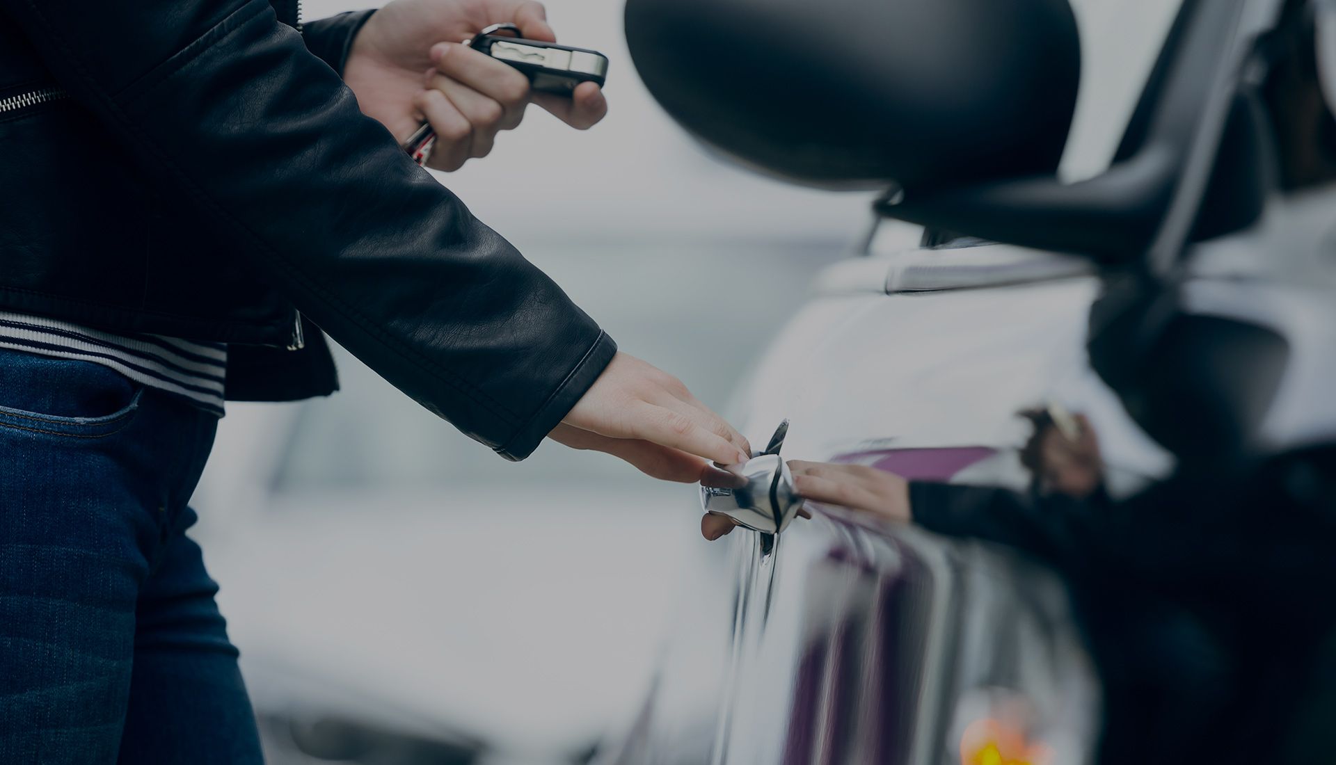 A person is holding a car key in front of a car.