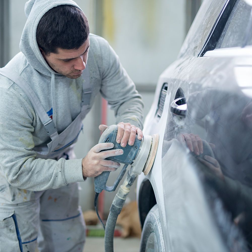 A man is sanding a car with a sander in a garage.