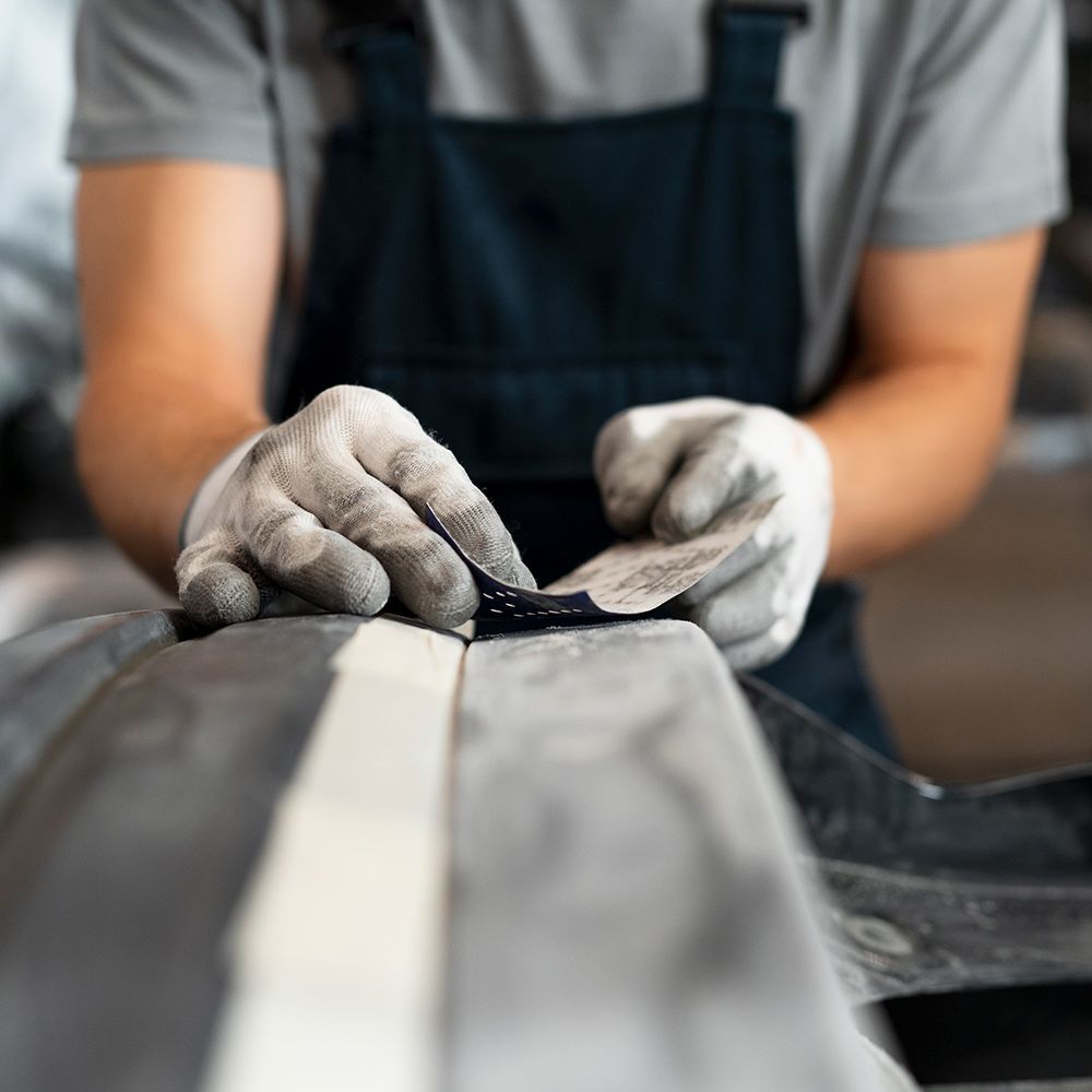 A person wearing gloves is sanding a piece of metal.