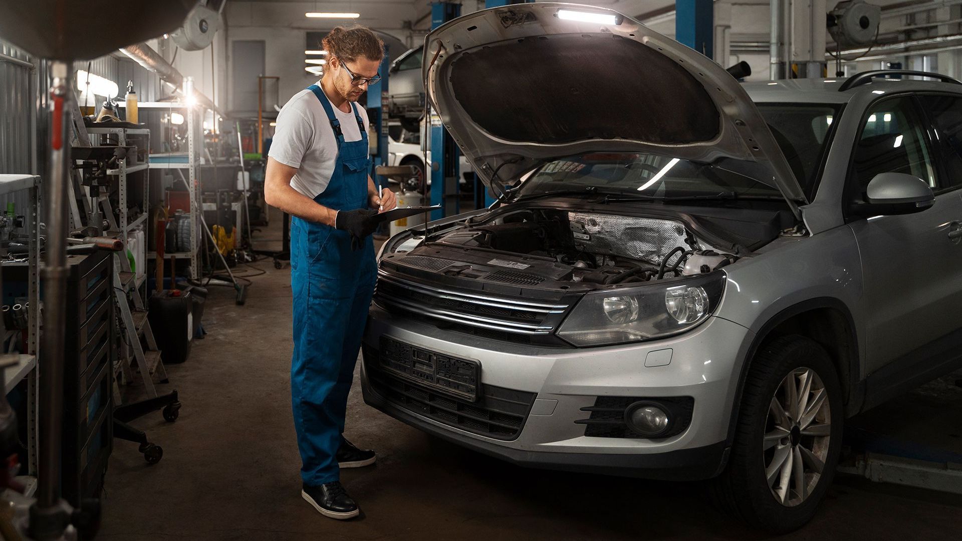A mechanic is working on a car in a garage with the hood open.