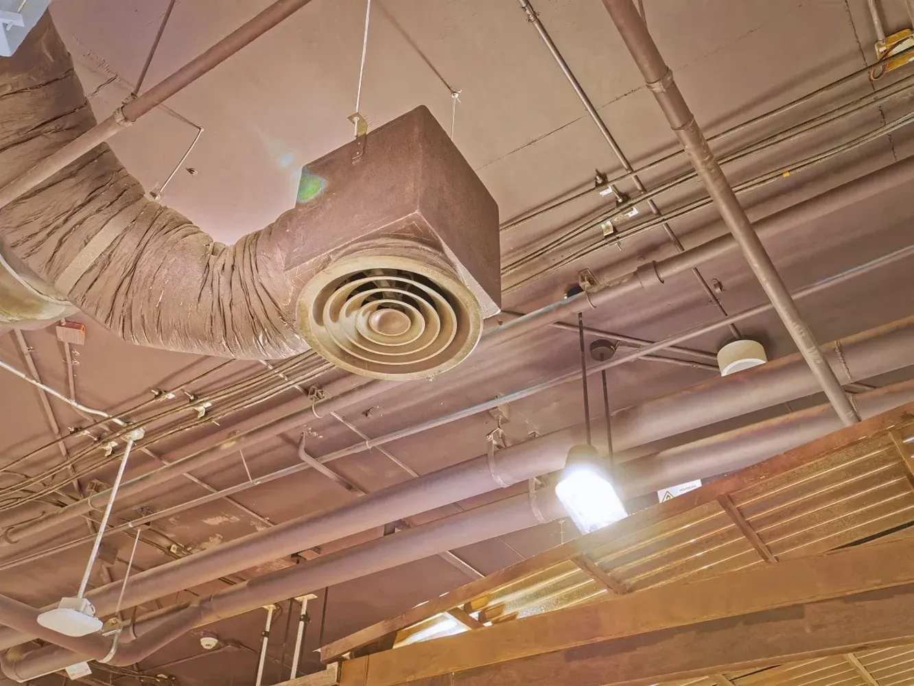 Brown industrial ceiling with ventilation and piping, lit by overhead lights.