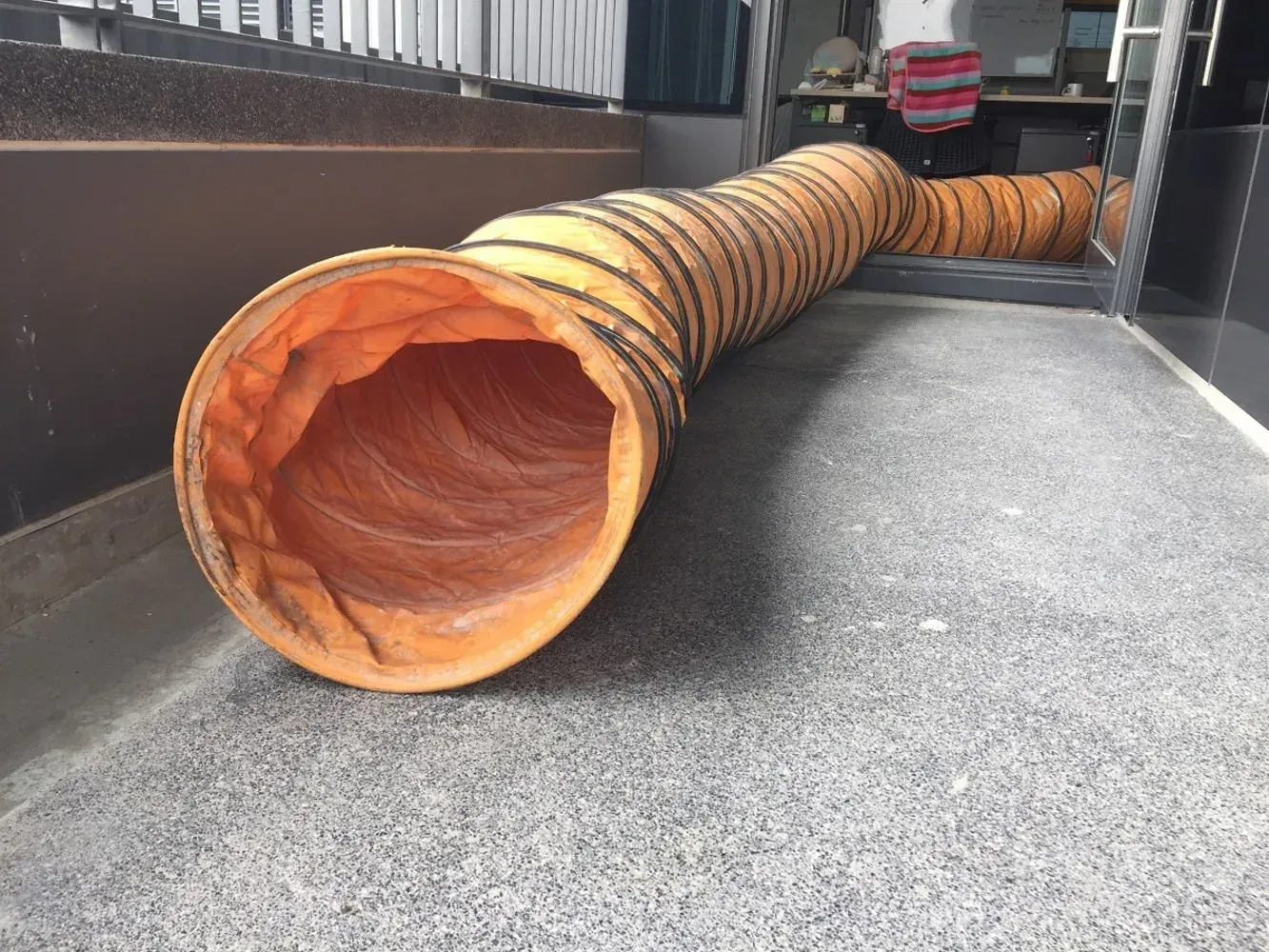 Orange flexible ventilation duct on gray floor, leading to unseen area.