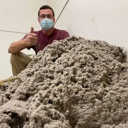Man in mask gives thumbs up near a large pile of insulation. Indoors, neutral color.