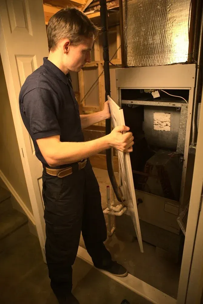 Man inspecting furnace, removing panel, in basement.