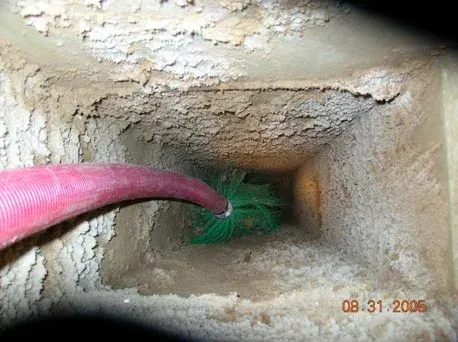 Inside view of a dusty chimney with a red hose and green brush for cleaning.