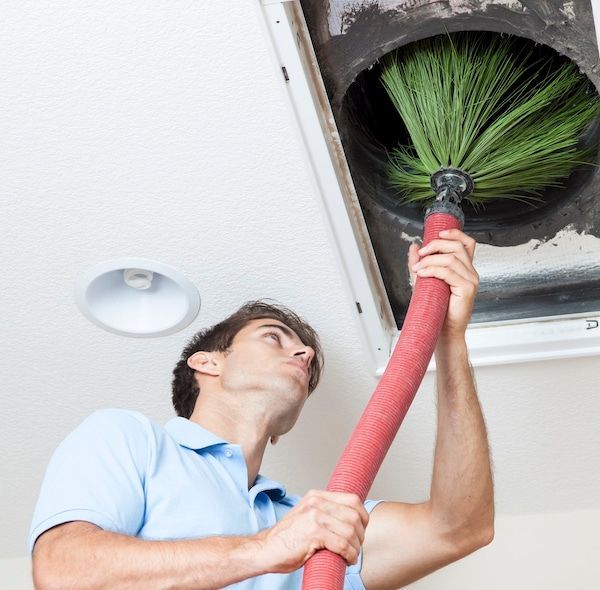 Man on a ladder cleaning a ceiling vent, wearing gloves and a face mask in an office.