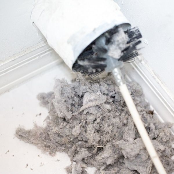 Man cleaning air duct with rotating brush tool in ceiling.