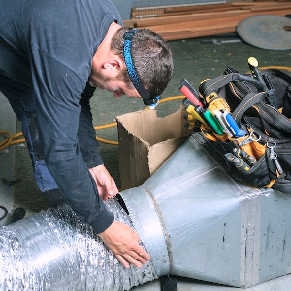 Person working on ventilation ductwork; using a knife, wearing a headlamp, tools nearby.