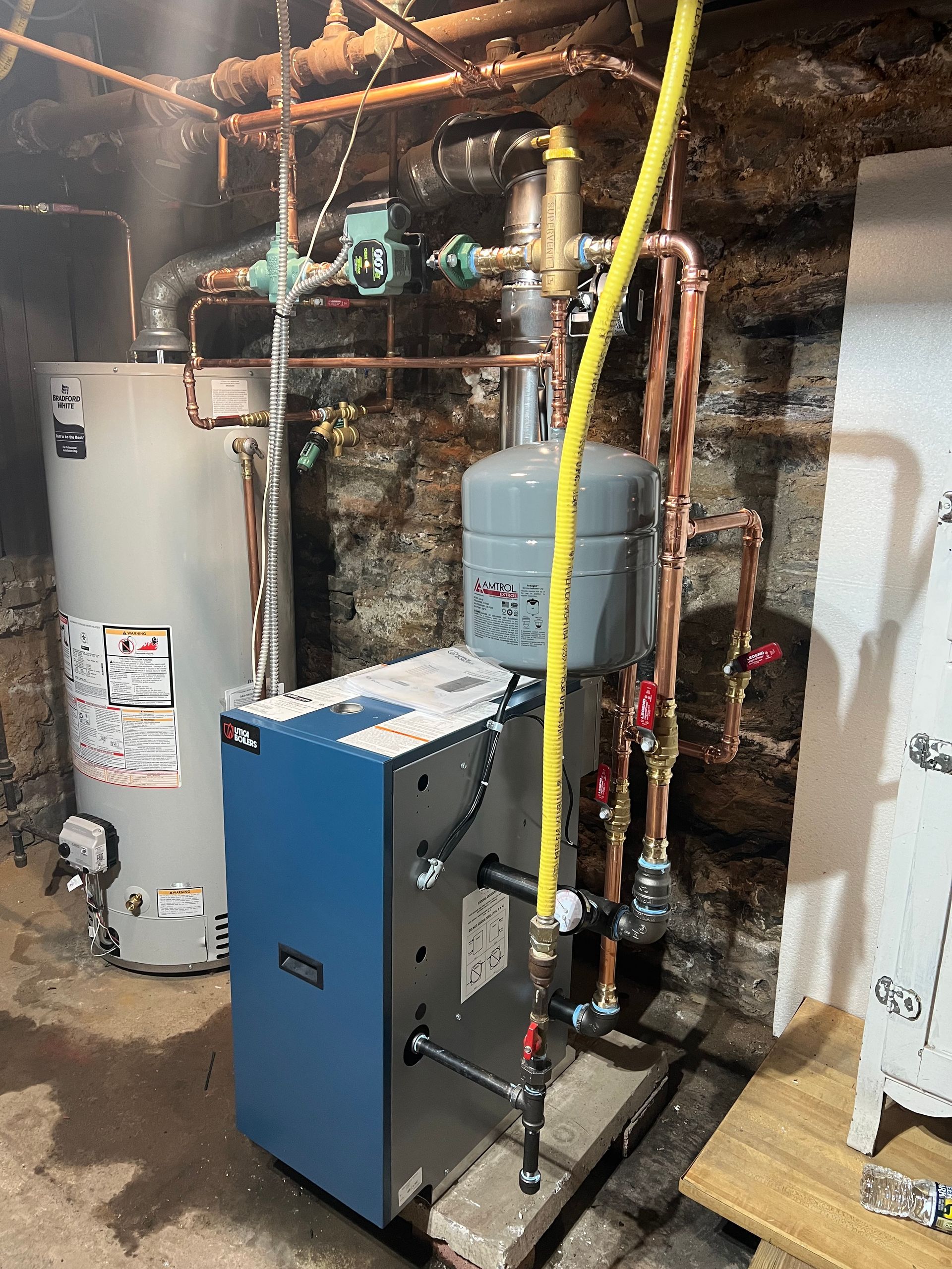 A water heater is sitting in a corner of a room next to a ladder.