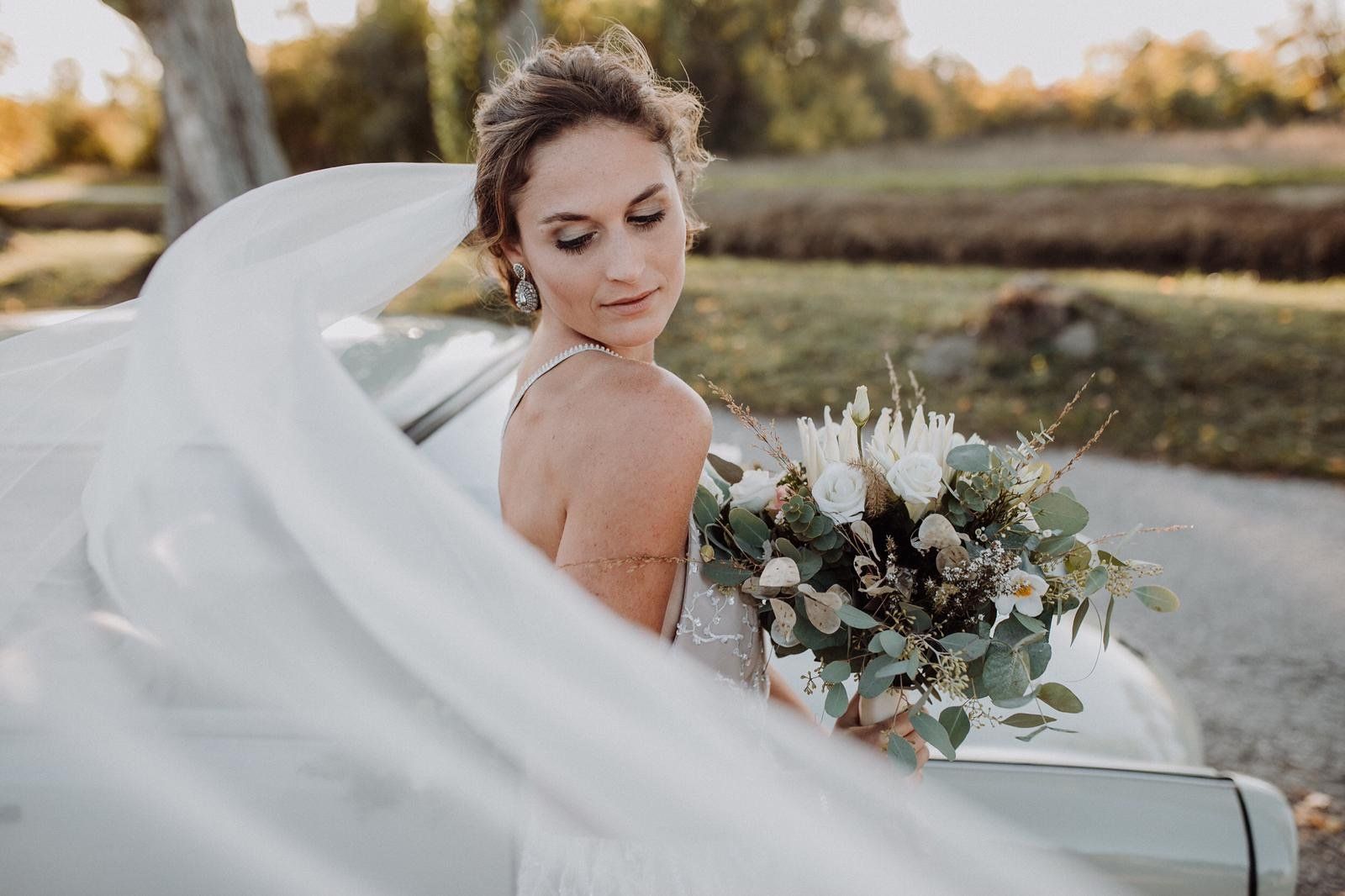 Eine Braut hält einen Blumenstrauß und steht neben einem Auto .