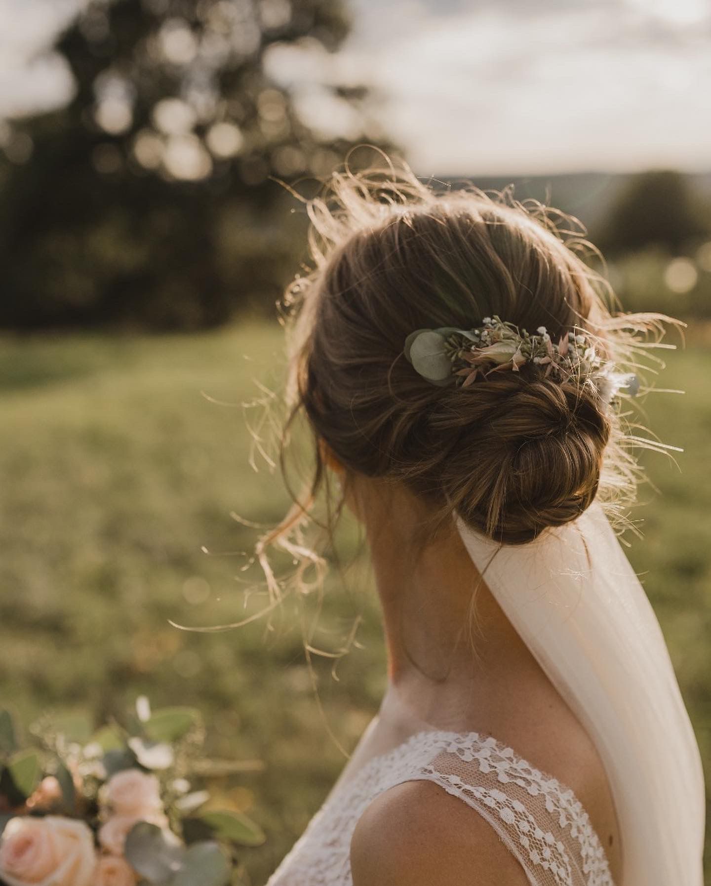 Eine Braut in einem Brautkleid und Schleier steht auf einem Feld.