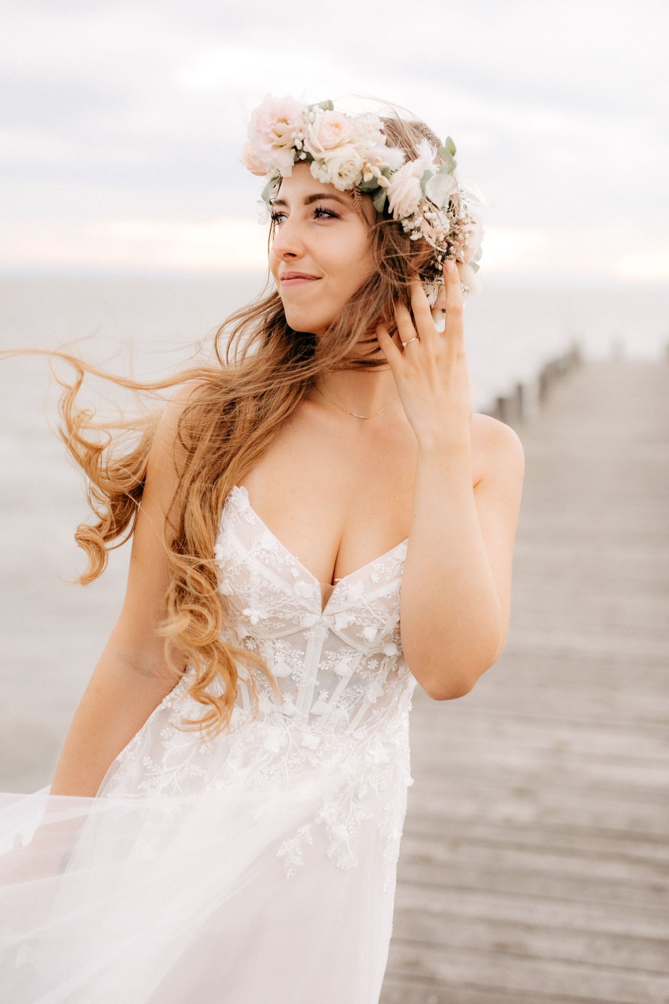 Eine Frau in einem Brautkleid und einem Blumenkranz steht auf einem Pier.